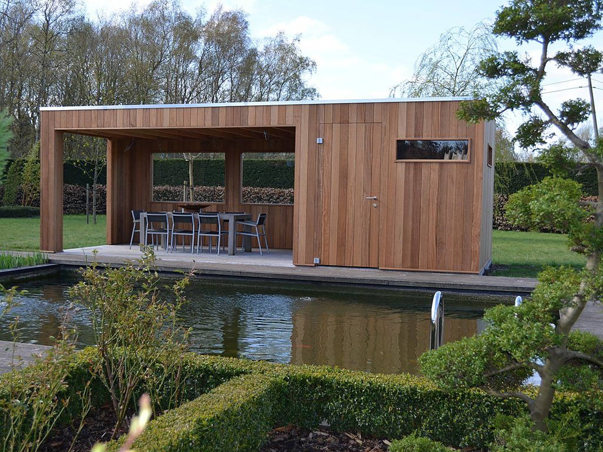 Poolhouse met verticale houten gevelbekleding en overdekte eethoek aan een zwemvijver