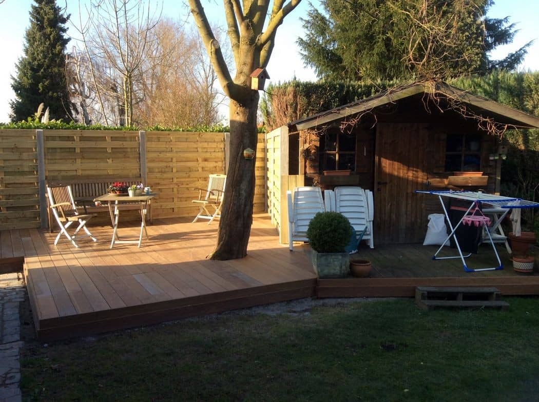 Houten terras rond een bestaande boom, met tuinhuis op de achtergrond